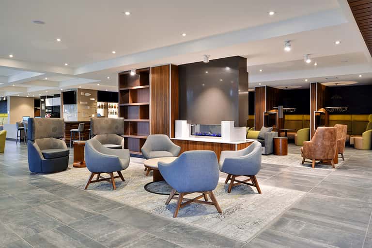 Modern hotel lobby with curved blue chairs, wooden shelving, fireplace, and ambient lighting