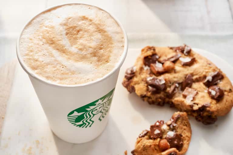 Starbucks latte with cinnamon topping next to chocolate chip cookies