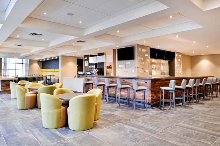 Casual hotel bar and lounge with yellow seating, wood accents, and high ceiling