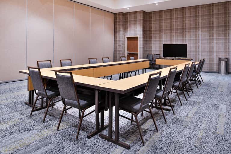 U-shaped conference table with chairs in meeting room with patterned walls and wall-mounted TV