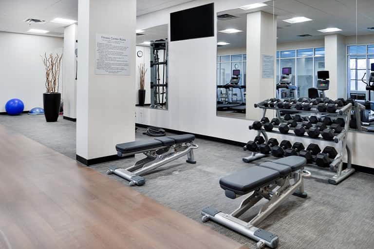 Modern fitness center with dumbbells, weight benches, exercise equipment, and mirrors