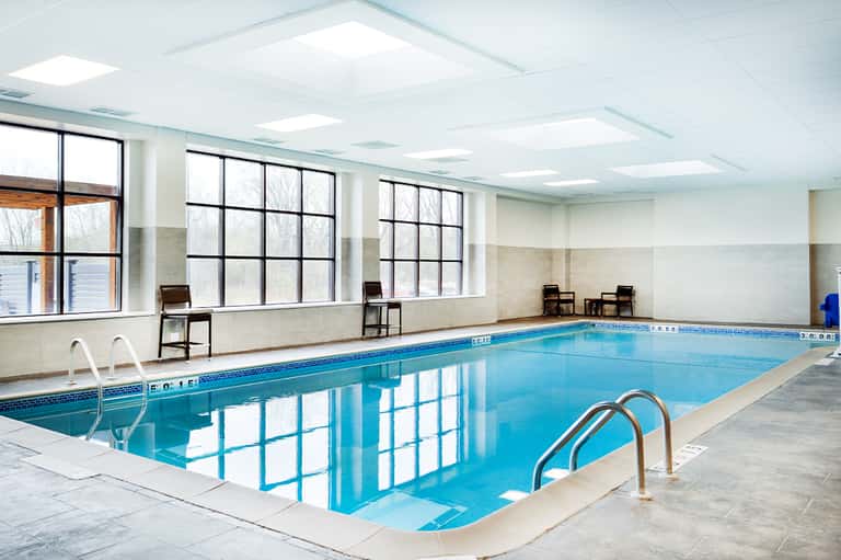 Indoor lap pool with bright blue water, white ceiling with skylights, and large windows along the side
