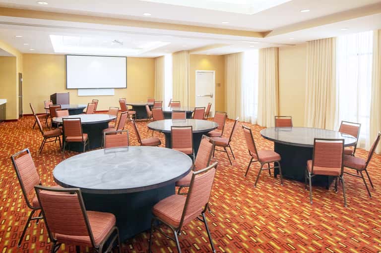 Conference room with round tables, coral chairs, orange patterned carpet, and projection screen