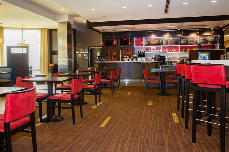 Modern hotel restaurant and bar with red chairs, black tables, and open kitchen concept