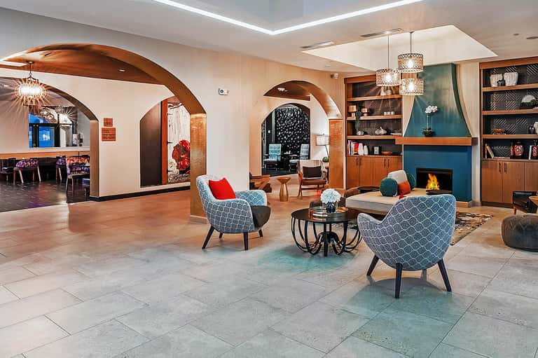 Modern resort lobby with arched wooden ceilings, fireplace, geometric armchairs, and built-in shelving.
