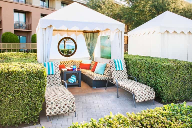 Upscale outdoor lounge area with white cabanas, patterned seating, and colorful accent pillows under umbrellas.