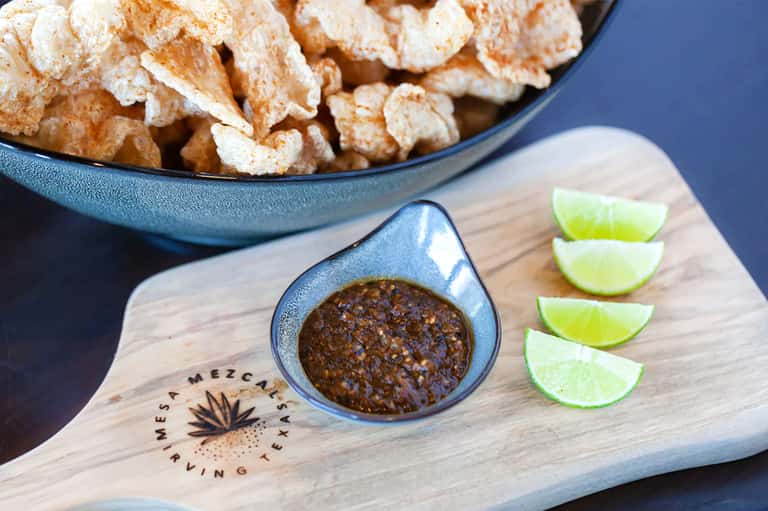 Bowl of tortilla chips with salsa and lime wedges on wooden serving board