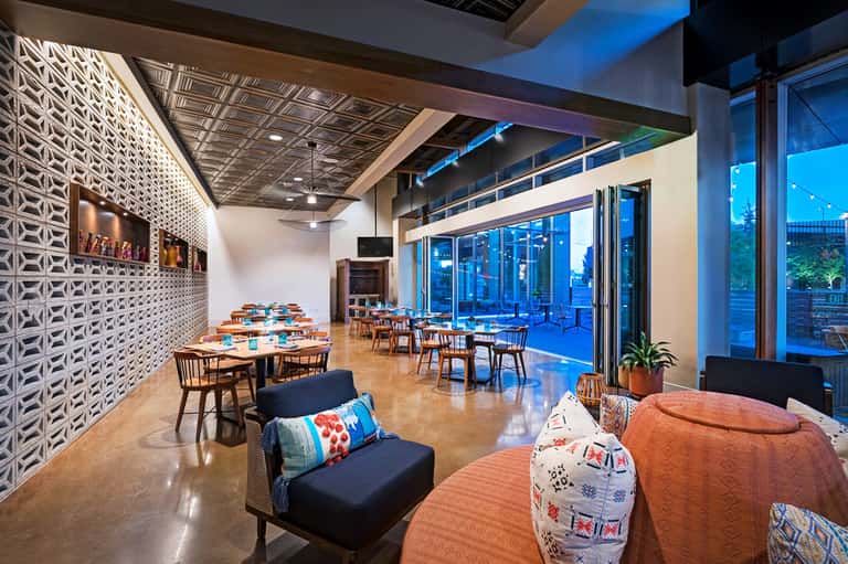 Modern restaurant and lounge with geometric wall panels, floor-to-ceiling windows, and city views