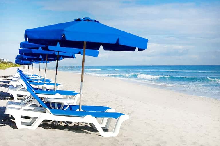 Beach with rows of blue and white lounge chairs and umbrellas along sandy shore