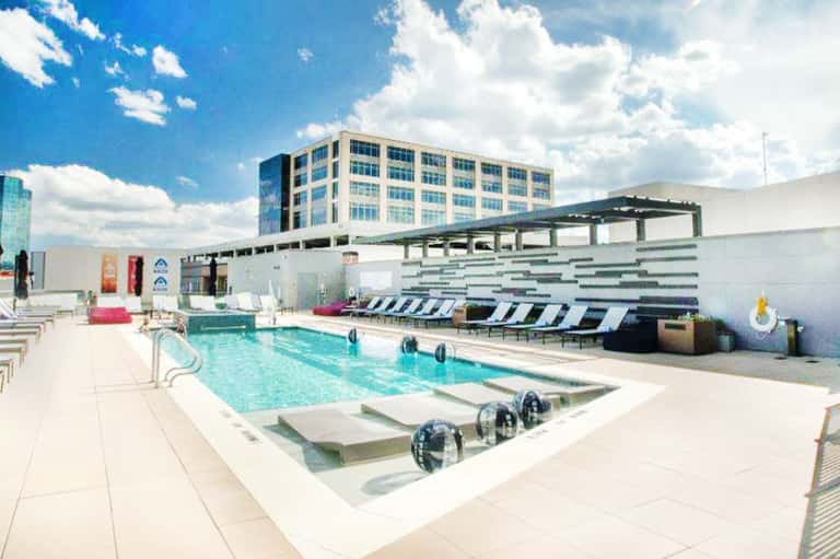 Modern rooftop pool with turquoise water, lounge chairs, white pergola, and multi-story hotel building