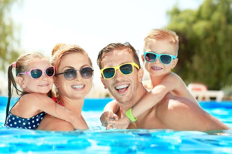 Family of four swimming in bright blue pool wearing colorful sunglasses