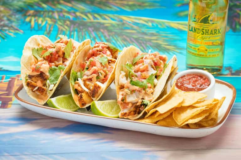 Three fish tacos with cilantro and lime on white plate with chips and salsa