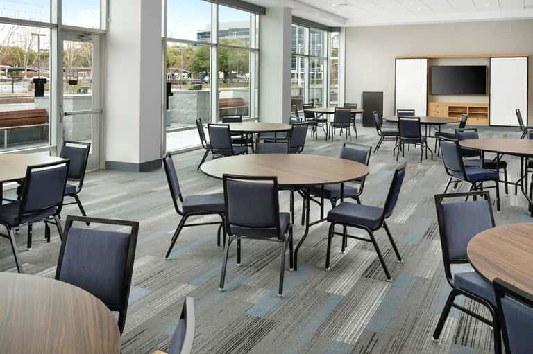 Contemporary hotel gathering space with round tables, comfortable seating, and large windows