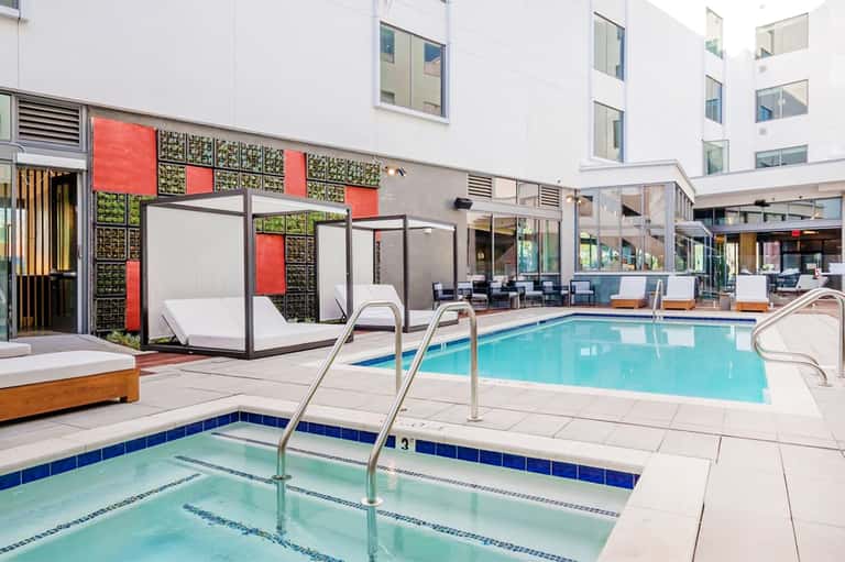 Indoor resort pool with colorful modular cabanas, modern lounge seating, and multi-story white building backdrop