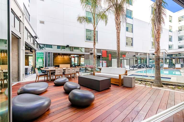 Modern resort courtyard with lounge seating, fire pit, and pool area surrounded by palm trees