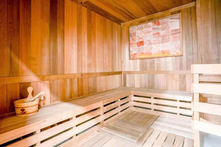 Light wood sauna with cedar paneling, wooden benches, salt therapy decorations, and traditional sauna aesthetic