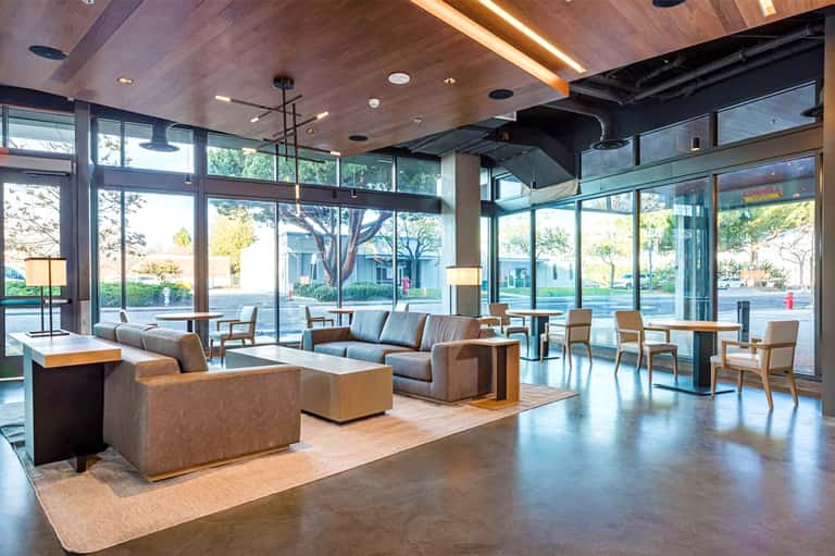 Modern hotel lobby lounge with floor-to-ceiling windows, tan seating, and contemporary wooden ceiling design