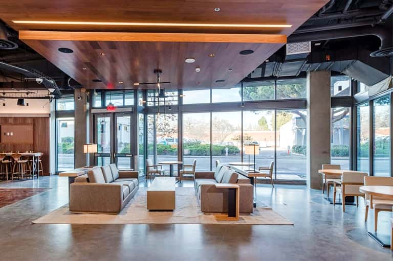 Modern hotel lobby with brown seating, wooden ceiling beams, and floor-to-ceiling windows