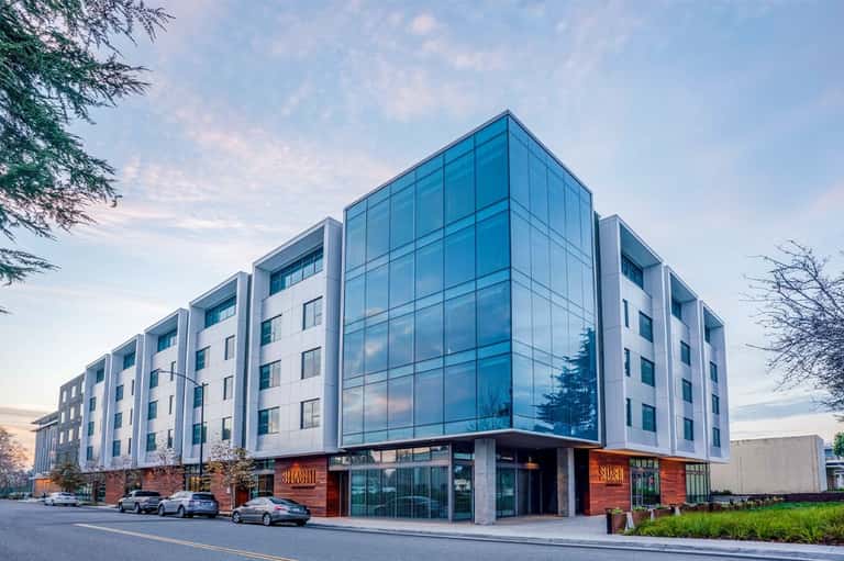 Contemporary multi-story hotel building with blue glass facade and ground-floor retail entrance