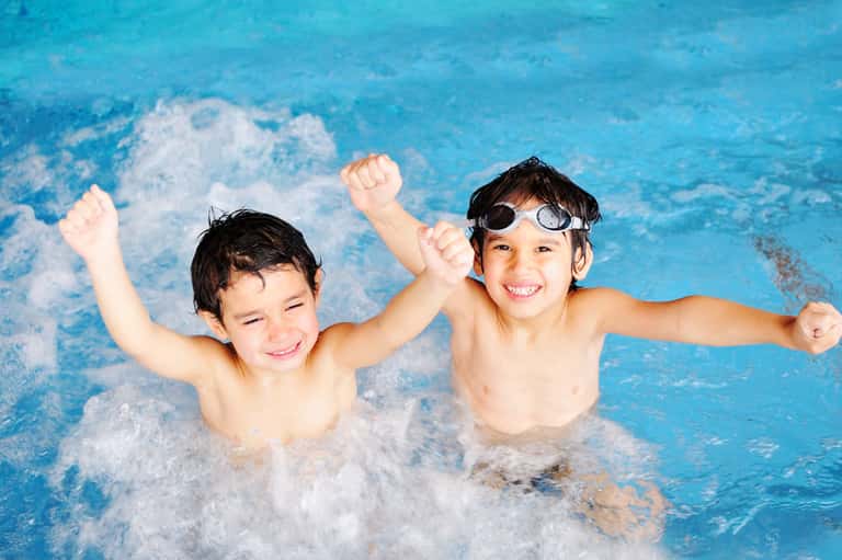 Two young boys smiling and playing together in a bright blue resort swimming pool