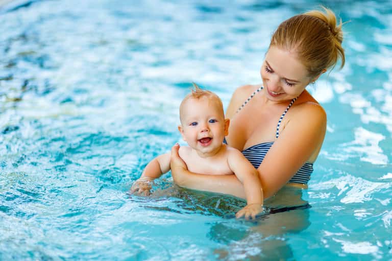 Mother and baby in pool together, smiling during water activity at resort