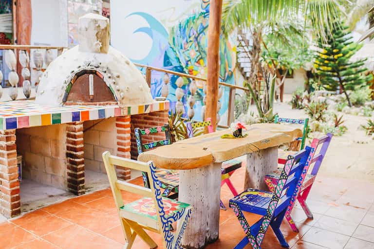 Colorful outdoor dining area with pizza oven, painted chairs, and tropical plants