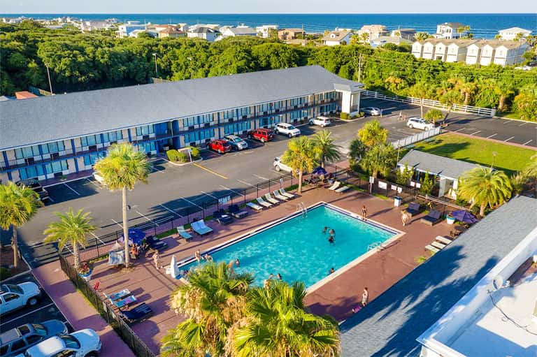 Beachfront hotel aerial view with turquoise pool, palm trees, oceanview rooms, and coastal landscape