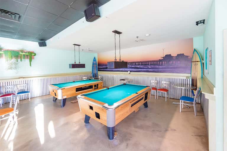 Game room with two blue pool tables, beach mural, and casual seating