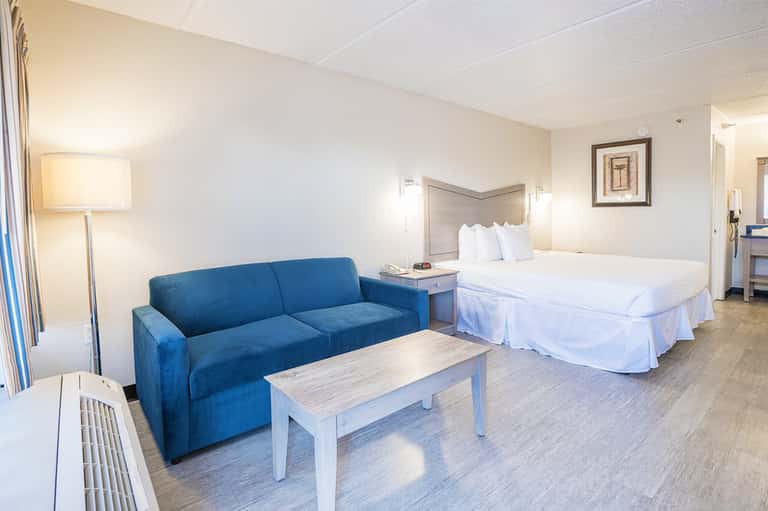 Hotel room with blue sofa, queen bed with white linens, and wooden flooring