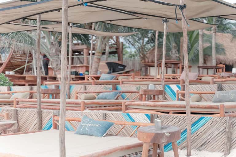 Beach cabana with wooden posts, shade canopy, striped cushions, and palm trees at sunset