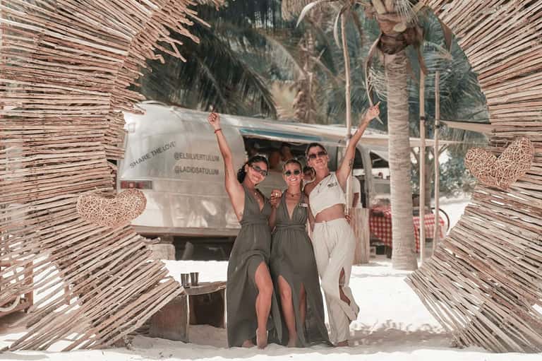 Three women posing at beach gate structure with palm trees and tropical vacation setting