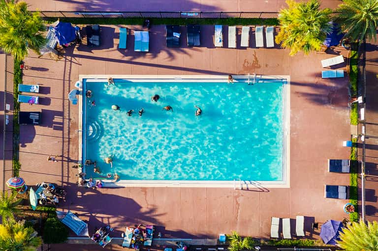 Overhead view of rectangular pool surrounded by striped beach chairs and palm trees