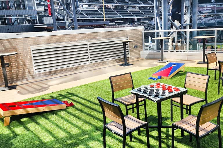 Outdoor recreation area with cornhole, checkers game, and grass overlooking stadium