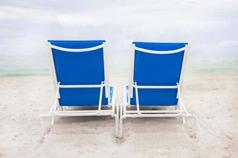 Two blue and white beach chairs facing the ocean on sandy shore with calm waves