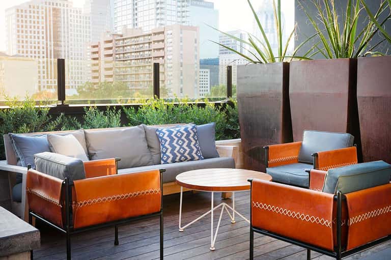Rooftop lounge with orange leather chairs, gray sofa, white table, and city skyline view with potted plants