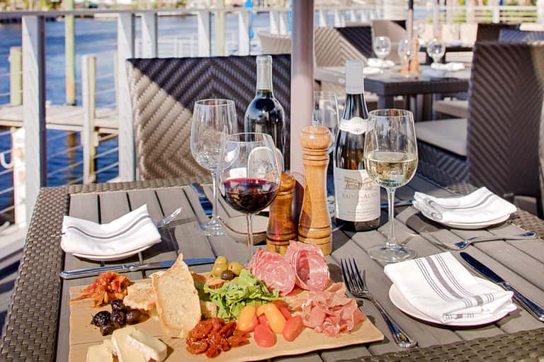 Waterfront dining table set with wine, appetizers, glasses, and ocean view in background