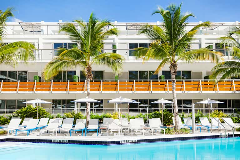 Modern beachfront hotel exterior with white balconies, orange accents, and palm trees