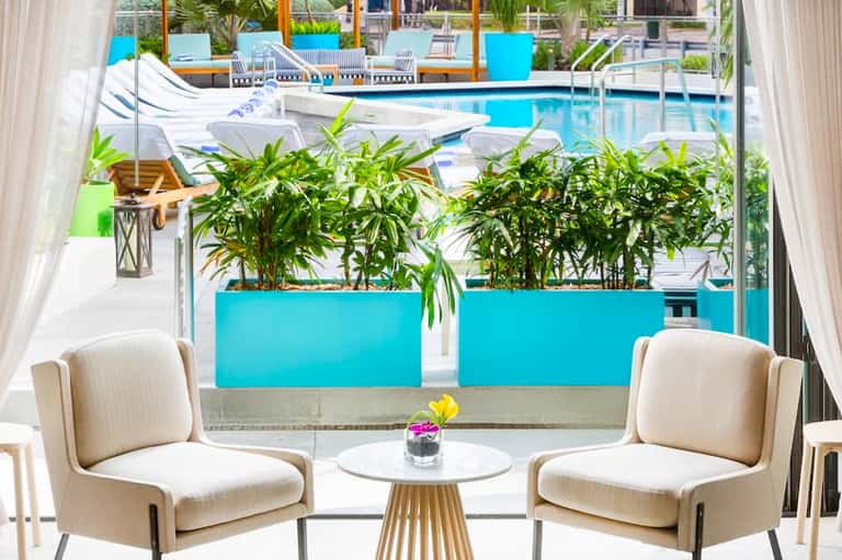Modern lounge seating with view through glass doors to pool with bright blue planters and palm trees