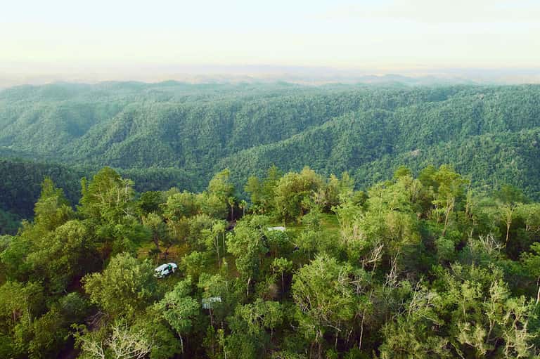 Aerial view of lush green forested hills and valleys with white vehicle visible on a road