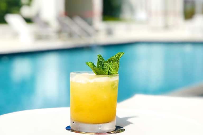 Bright yellow cocktail with mint garnish beside a swimming pool on a sunny day