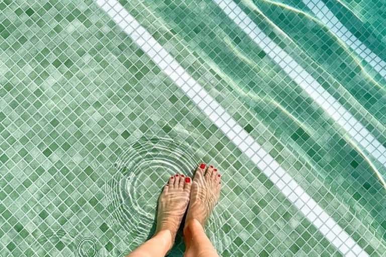 Feet dangling in green-tiled pool with rippling water and white lane divider