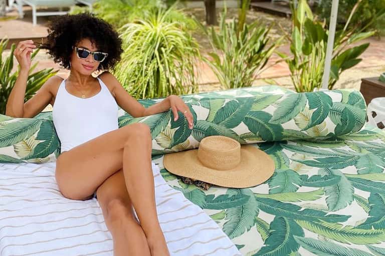 Woman relaxing on tropical leaf-patterned lounger by beach with palm plants and straw hat
