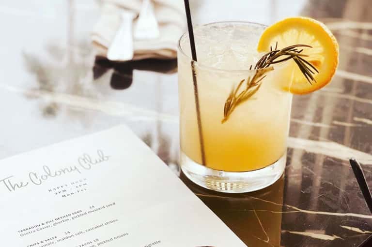 Craft cocktail with lemon slice and rosemary garnish on a table with menu at upscale restaurant