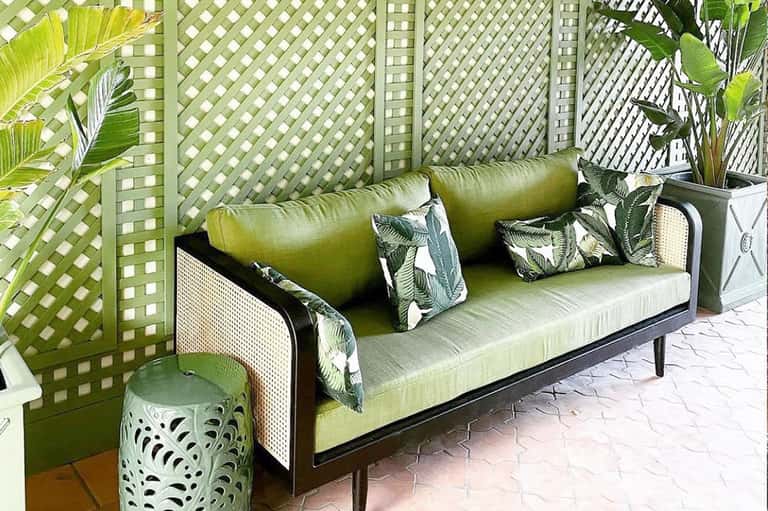 Green outdoor seating nook with patterned pillows, lattice privacy screen, and tropical plants