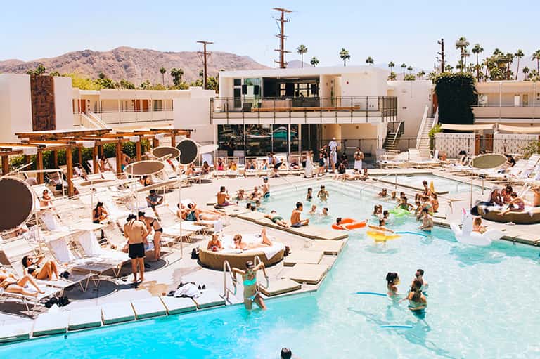Modern resort pool with loungers, umbrellas, and mid-century architecture on sunny day