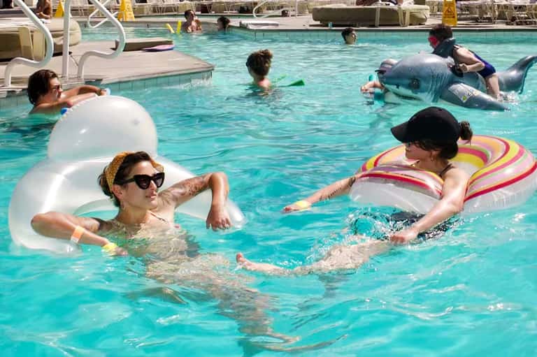 Resort pool with guests swimming, inflatable floats, and lounge seating
