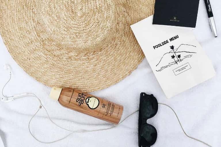 Poolside essentials: straw hat, sunscreen, sunglasses, menu, and earbuds on white towel