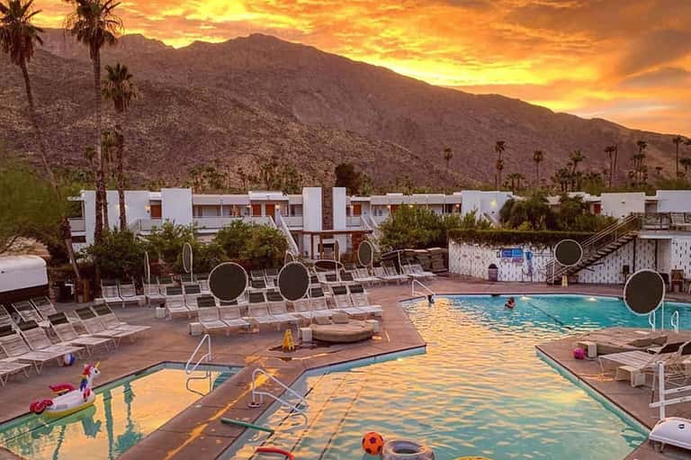 Resort pool at sunset with mountain backdrop, white loungers, and modern accommodations