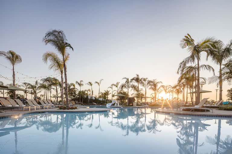 Resort swimming pool at sunset surrounded by palm trees and lounge chairs with clear reflections