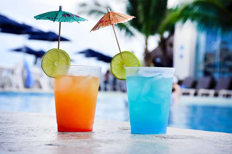 Two colorful cocktails with umbrella garnishes and lime slices on pool deck at twilight